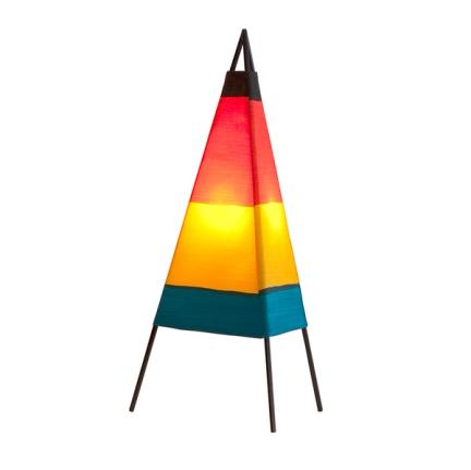 A triangular lamp sits against a white background. It has three, black, wire metal legs arranged in a triangle and coming to a point at the top. The fabric yardage forms the lamp shade and has a horizontal teal stripe at the bottom, yellow above the teal, red above the yellow, and a thinner black stripe at the top.