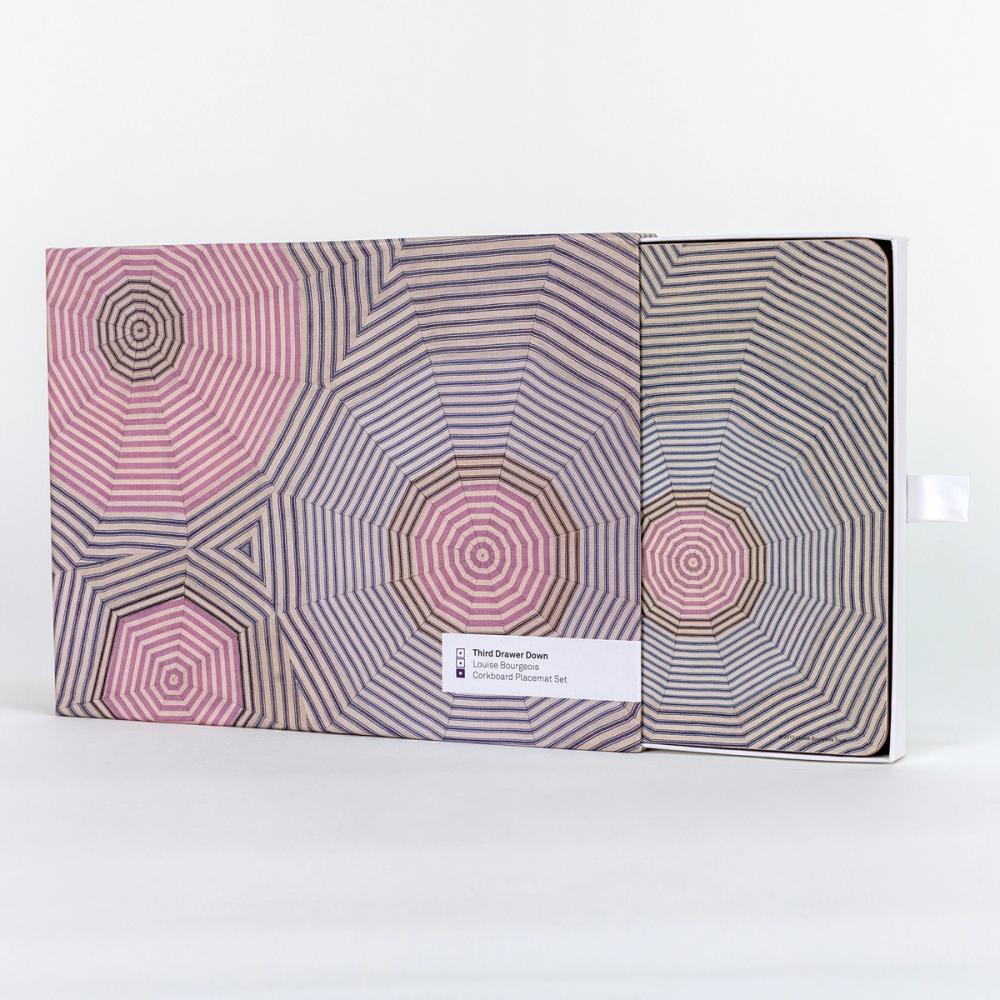 A box featuring a design of striped fabric cut into triangles and arranged to create a 12-sided circle-like shape. The box has been slid open where the viewer can see a hard placemat featuring the same image inside.