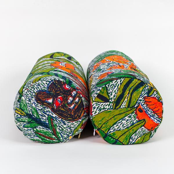 Two long cylindrical pillows positioned side by side, stretching away from the camera so that the viewer is facing the circular ends of them. The pillows features a colorful pattern of leafy foliage, flowers, and wild creatures.