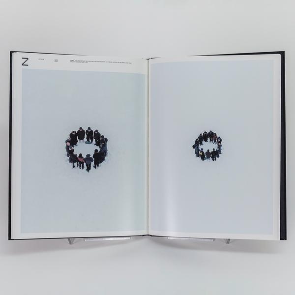 A photograph of an open book. On the left there is a large photo of a group of people in warm and dark clothing standing in a circle surrounded by snow. On the left is a similar photograph but more zoomed out.