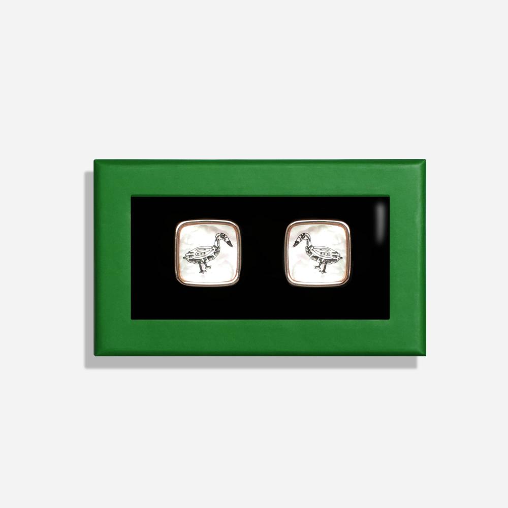 A rectangular box with a green border features a pair of square white pearlescent cufflinks with a rose gold border and clips. On the pearlescent face is a black line illustration of a Bata bird.