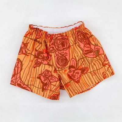 An image of boxer shorts against a white background. The shorts are a light orange with pink and brighter orange patterns and brown details and outlines. The print design on the boxers shows line drawn imagery of roses, butterflies, and faces.