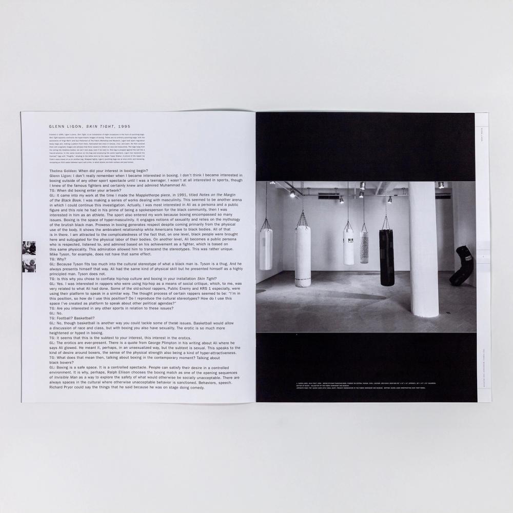 A photograph of an open paperback book spread. On the left is text featuring an interview. On the right is a large black and white photograph of five black and white punching bags hanging at various heights and distance within a gallery setting. There is one black punching bag sitting upright, but slumped against the right-side gallery wall.