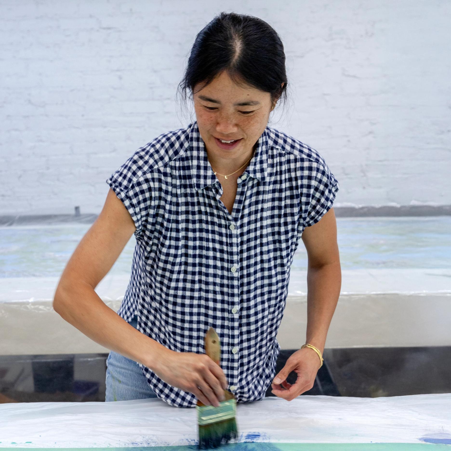 A woman standing over a table brushing pigment onto a cloth
