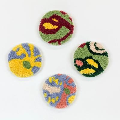 A selection of four circular tufted coasters in different colorways on a white ground. The abstract design of the coasters features organic lines and shapes in greens, maroon, yellow, light blue, and peach.