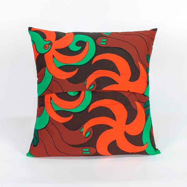 The back of a square pillow made of fabric featuring a repeating textile pattern with stylized green snakes intertwined with abstract brown shapes and bright orange spirals on a dark brown background. The top and bottom panels of fabric overlap in the center to create an opening.