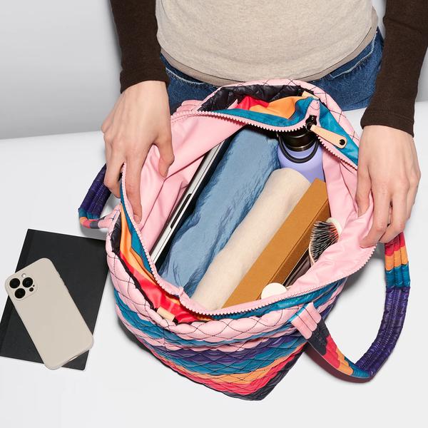 A picture of a person spreading a bag open to show its interior contents, which includes a laptop, thermos, a hair brush, and other things.