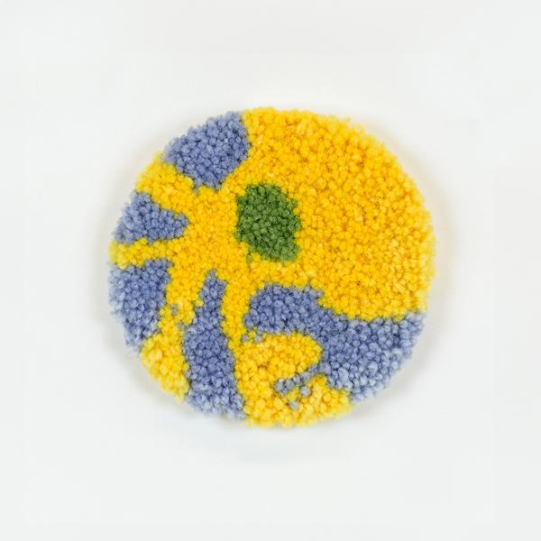 A tufted coaster featuring an abstract design of organic lines and shapes in light blue, yellow, and light green.