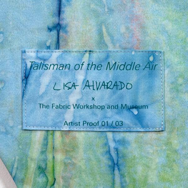 A colorful textile wall hanging with three overlapping diamond-shapes made of fabric that has been dyed in a painterly way in blue, brown and green. Inside there is a sheer green diamond. There is a rectangle of the same dyed fabric sewn onto the diamond panel as a label of the banner with the artist's name and edition number.
