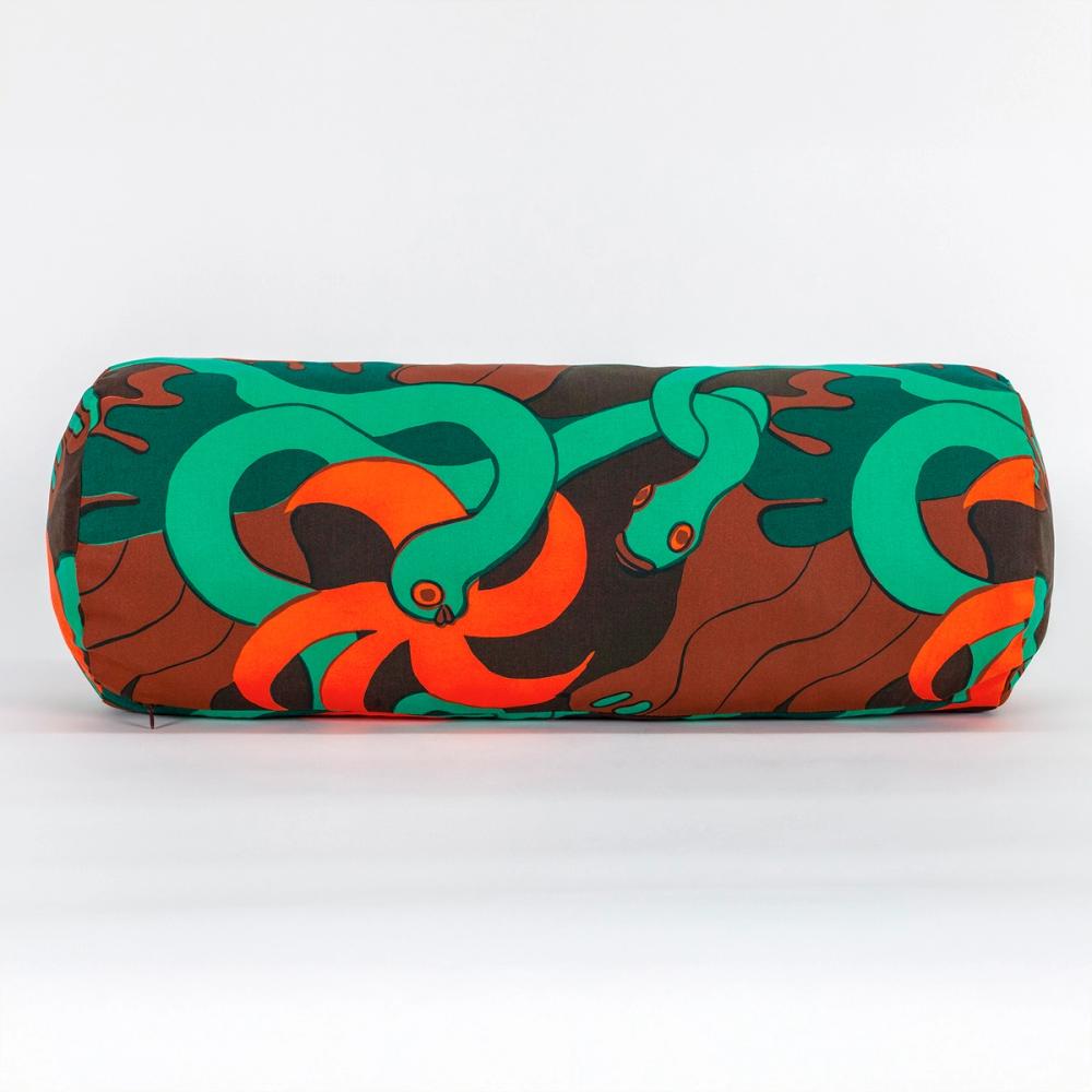 A long cylindrical pillow made of fabric featuring a repeating textile pattern with stylized green snakes intertwined with abstract brown shapes and bright orange spirals on a dark brown background.