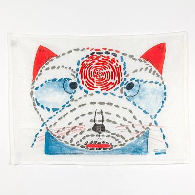 A rectangular piece of fabric with a painted image of a cat composed of individual brush marks arranged like embroidered stitches. The cat has red ears and a large red spot composed of swirling marks between its two large eyes. 