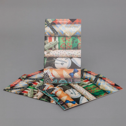 An image of a thin, rectangular book, more tall than it is wide. The cover of the book depicts a variety of colorful fabrics in various patterns.