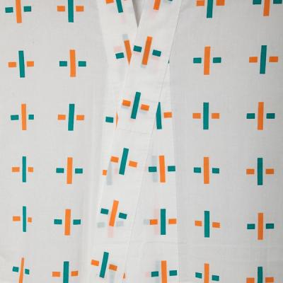 Close up image of a white yukata with cross designs adorning the garment in orange and green. The left side opening is laying on top of the right side showing the thinness and transparency of the fabric.