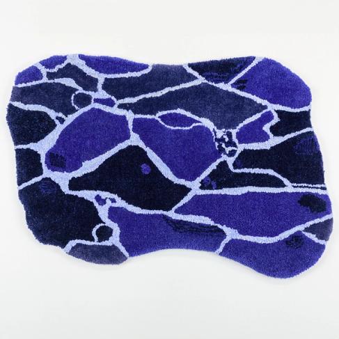 A photo of a blue rug of an organic, rectangular shape laying flat on a white background. The design of the rug is made up of different shades of blue, spanning from bright royal blue to dark navy. The shades are separated by a light blue and white outline, creating many organic shapes reminiscent of the surface of water.
