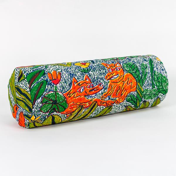 A long cylindrical pillow positioned at a 45-degree angle toward the camera. The pillow features a colorful pattern of leafy foliage, flowers, and two wild dogs.