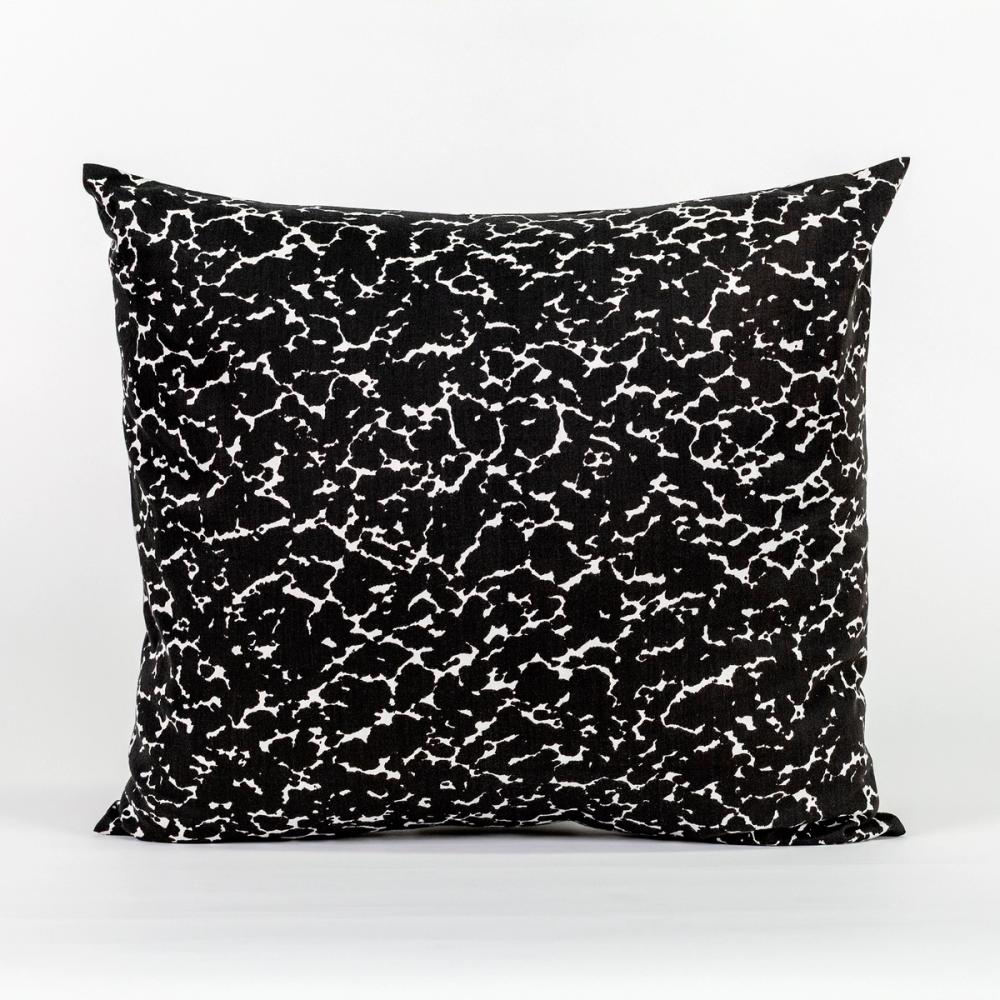 A square pillow featuring a speckled black and white design like the kind found on a student's composition notebook.