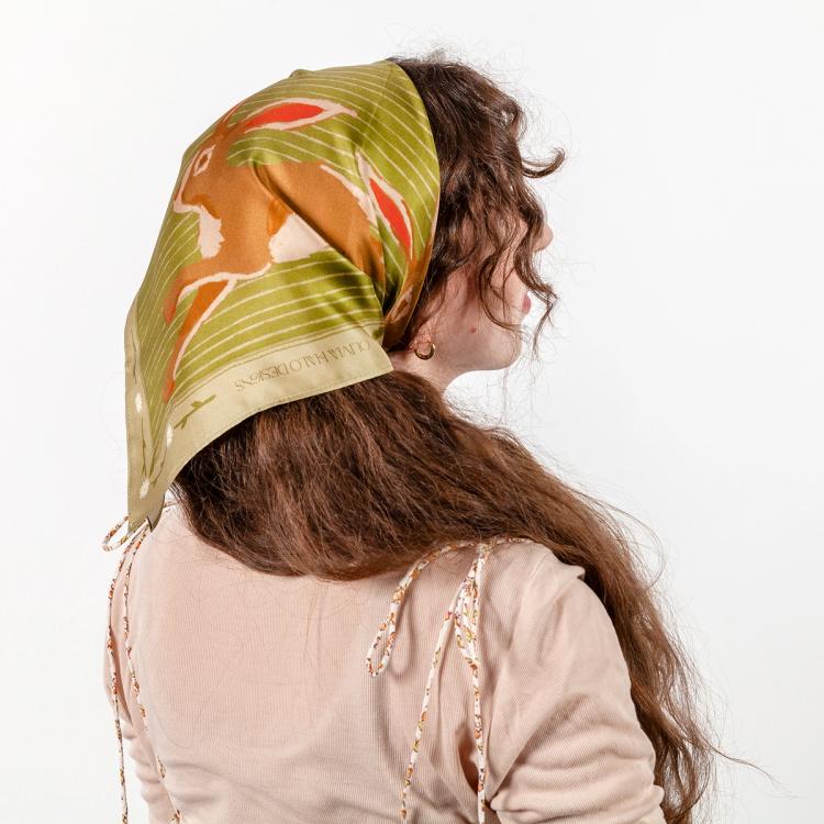 A photo of the back of a person with long hair wearing a digitally printed green silk scarf tied as a head bandana. There is an illustration of a brown rabbit on the scarf.
