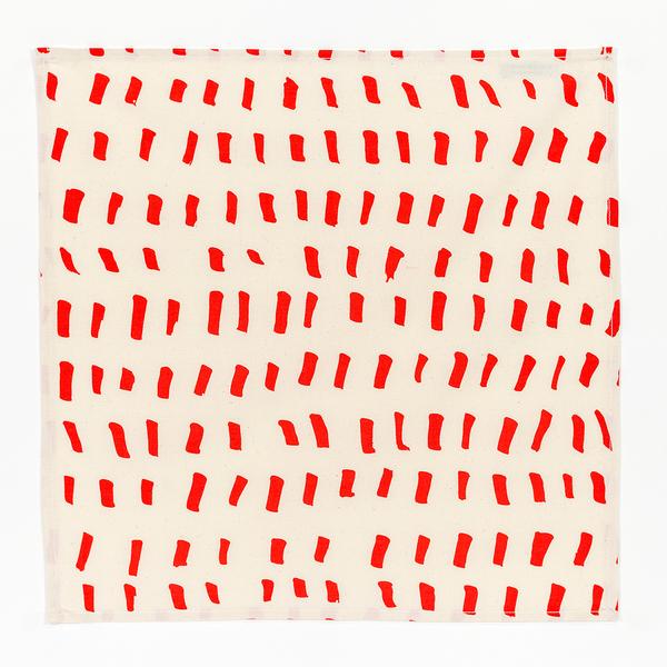 A square napkin composed of cream-colored fabric with several rows of short brushstroke-like red dashes.