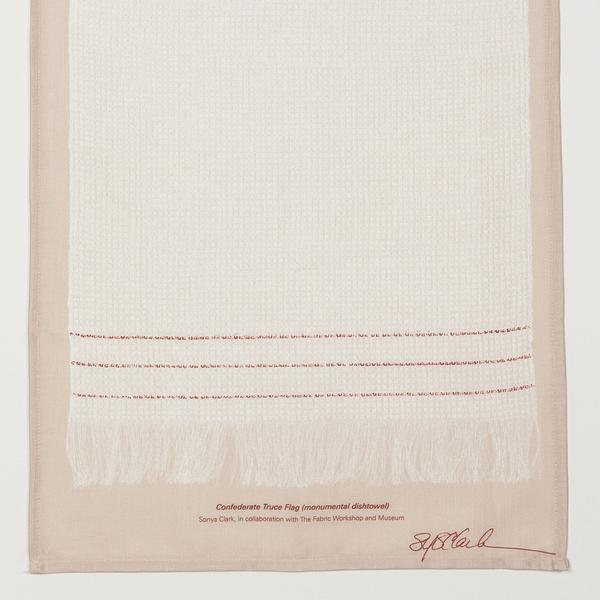 A detail of the lower portion of a print of a cream-colored dishtowel, longer than it is wide, with three red stripes and fringe on the bottom. The print is on a beige background and is signed by the artist, Sonya Clark. The text reads, "Confederate Truce Flag (monumental dishtowel). Sonya Clark, in collaboration with The Fabric Workshop and Museum. 