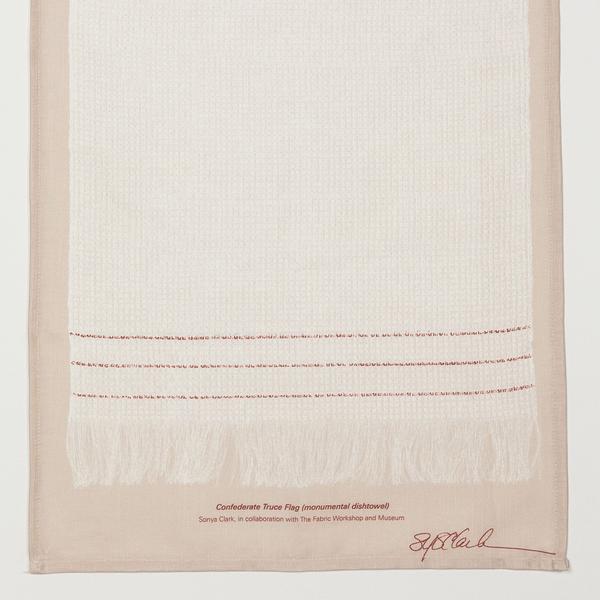 A detail of the lower portion of a print of a cream-colored dishtowel, longer than it is wide, with three red stripes and fringe on the bottom. The print is on a beige background and is signed by the artist, Sonya Clark. The text reads, "Confederate Truce Flag (monumental dishtowel). Sonya Clark, in collaboration with The Fabric Workshop and Museum.