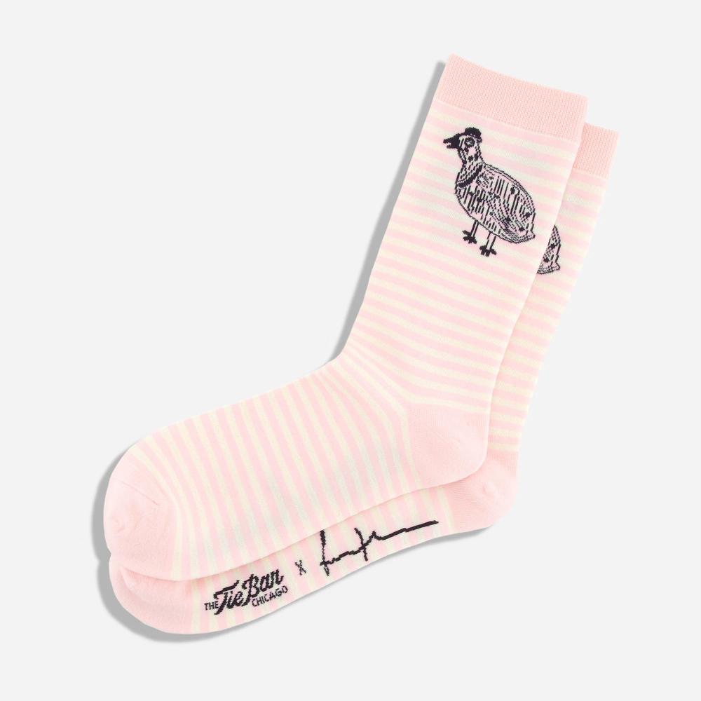 A pair of light pink and white striped knit dress socks with a black illustrated Kuku bird on the ankle of the socks. The artist's signature and "The Tie Bar" logo is featured on the bottom of the socks.