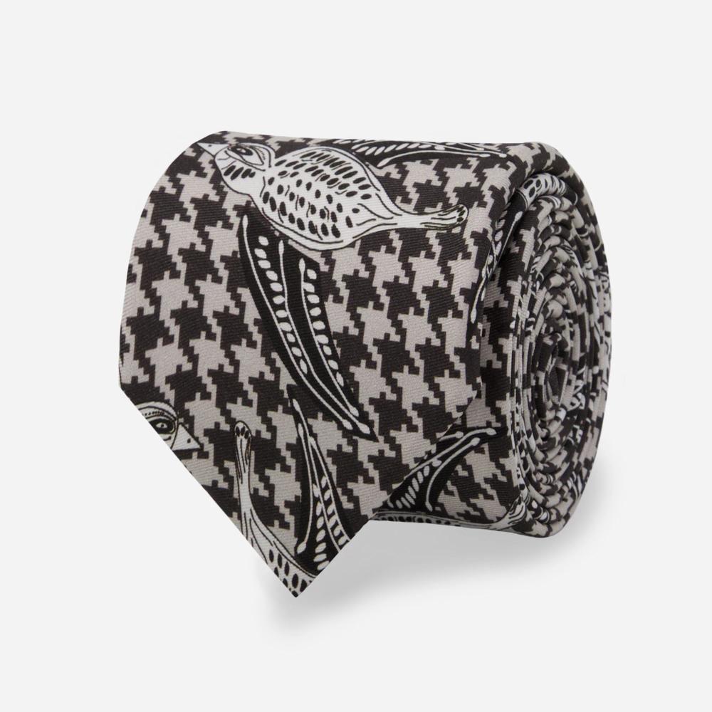 A detail of a rolled up tie with a pattern of black and white illustrated Shomoro birds flying in different directions on a light gray and black houndstooth background.