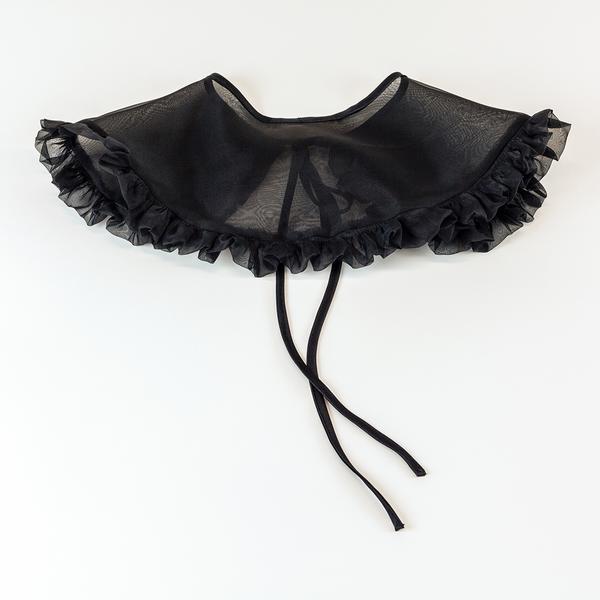 A black silk organza removable collar is lying with the back facing upwards flat against a white background. It is slightly sheer and has a ruffle around the outer edge.