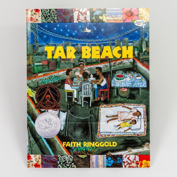 A photo of a hard cover book by Faith Ringgold titled "Tar Beach." The book cover is an illustration painted on a quilt of a family of 6 having dinner on a rooftop overlooking NYC and the George Washington Bridge.