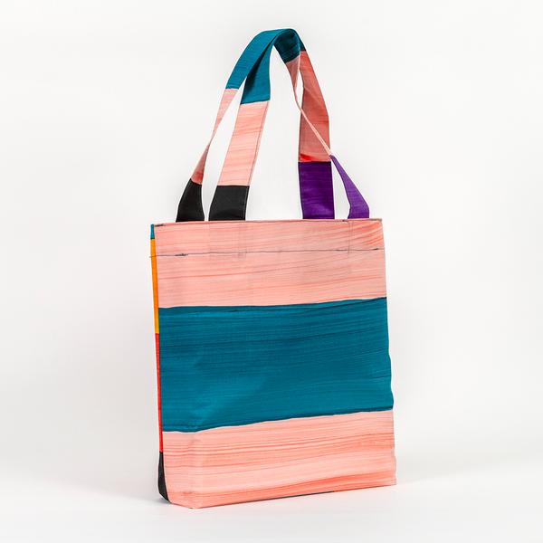 A tote bag taller than it is wide with straps about three-quarters of the bag's height. The bag features a pattern of thick stripes of peach, teal, purple, and black painted with the texture of brush strokes.