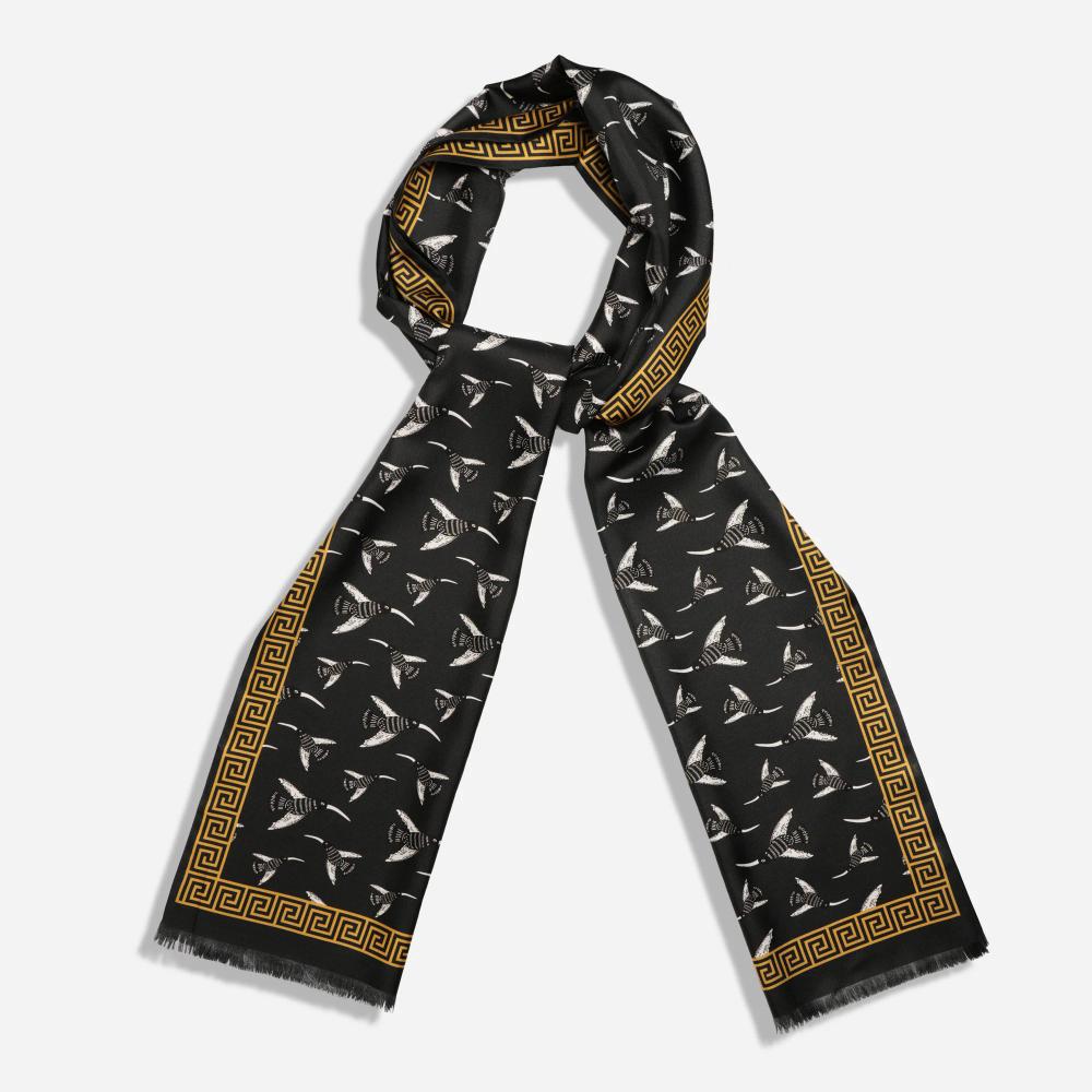 A long scarf is folded in a loop so as to allow space for a wearer's neck. Its gold border resembles a Greek-style spiral frieze. The interior pattern features illustrated birds with long beaks flying in different directions on a black ground.