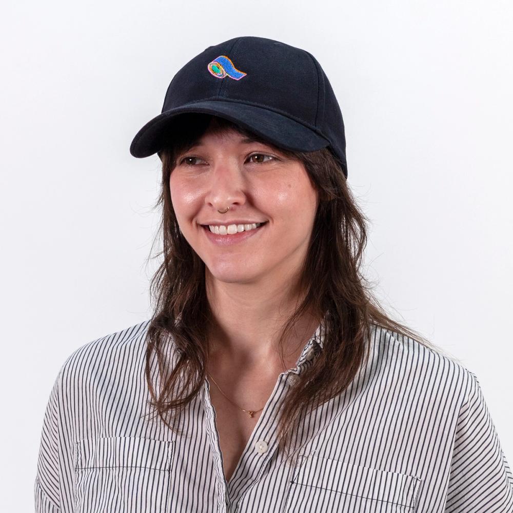 A photo of a model wearing a black baseball cap with an embroidery of blue tape. The center of the tape is green and there is a pink, yellow, and orange outline to the shape of the blue tape.