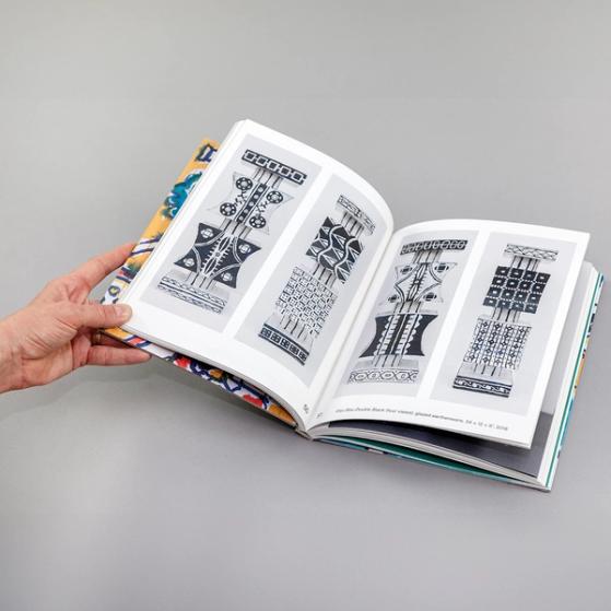 An image of a book spread featuring four photos of black and white painted totem-like pedestals decorated with different geometric patterns on each side. There are two images on each page.