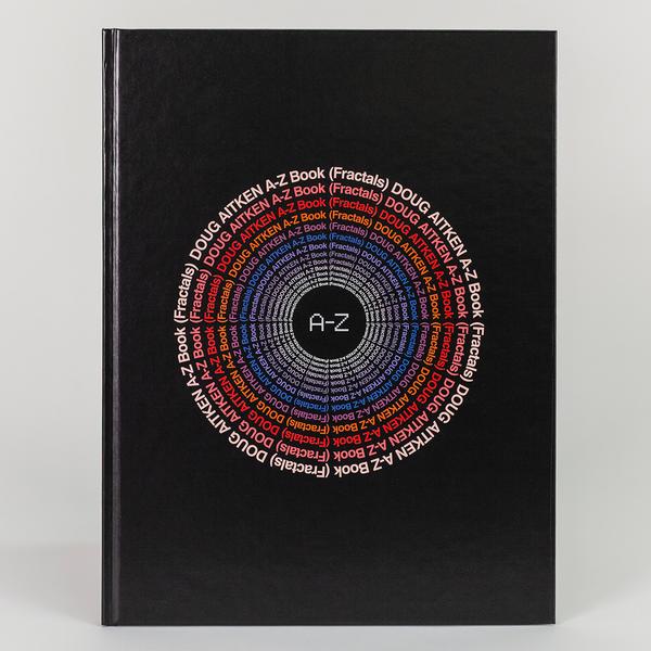 A photograph of a black hardcover book with the title "Doug Aitken A-Z Book (Fractals)" written repeatedly in a circle and echoing itself getting smaller towards the center. In the center is a black circle with "A-Z" written inside.