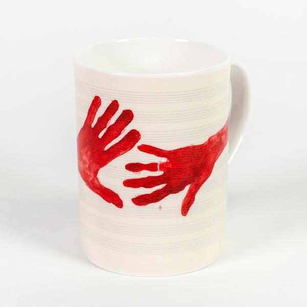 A tall cream colored mug featuring painted red hands with fingers outstretched. The hand on the right has a ring on its ring finger.