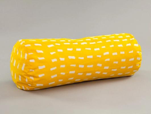 A long cylindrically shaped pillow laying on its side at a slight angle. It is bright yellow with an irregular pattern of short white streaks on all sides.