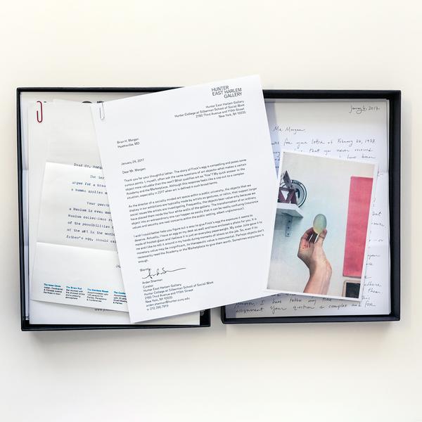 A black box sits open facing up against a white background. Stack of shuffled letters, each bundled with a paper clip, lie within the box's enclosure and overtop. To the right, a postcard-sized image features a hand holding an egg-shaped object near a shelf.