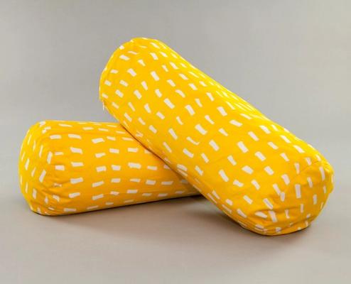 Two long cylindrically shaped pillows lay one on top of the other. They are bright yellow with an irregular pattern of short white streaks on all sides.