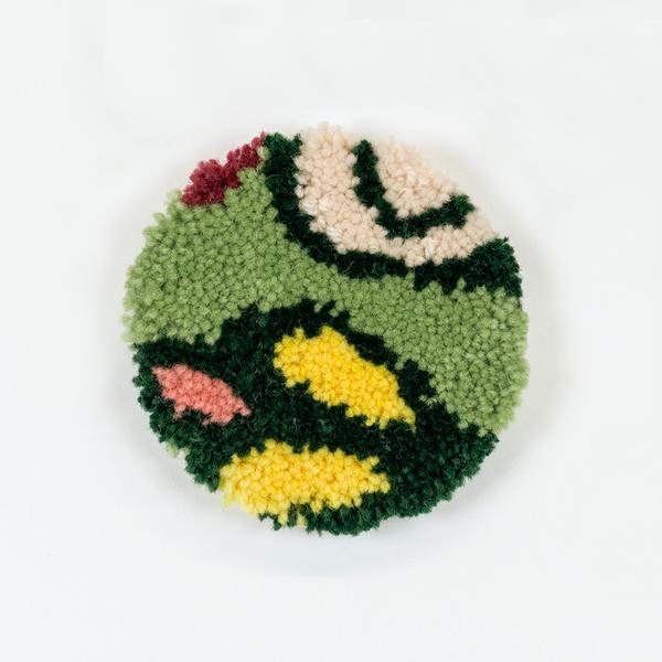 A tufted coaster featuring an abstract design of organic lines and shapes in light green, dark green, yellow, peach, and cream.