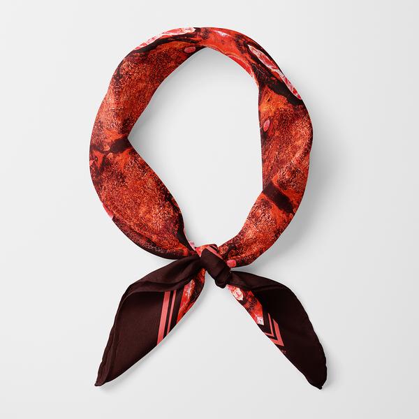 A thin red scarf with a mottled texture is tied into a ring so as to allow the neck of its wearer through it.