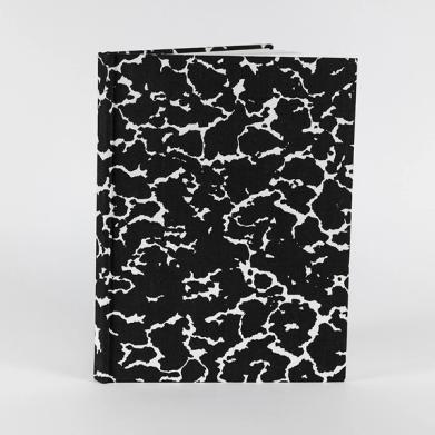 A sketchbook stands upright. Its cover features a black and white speckled pattern.