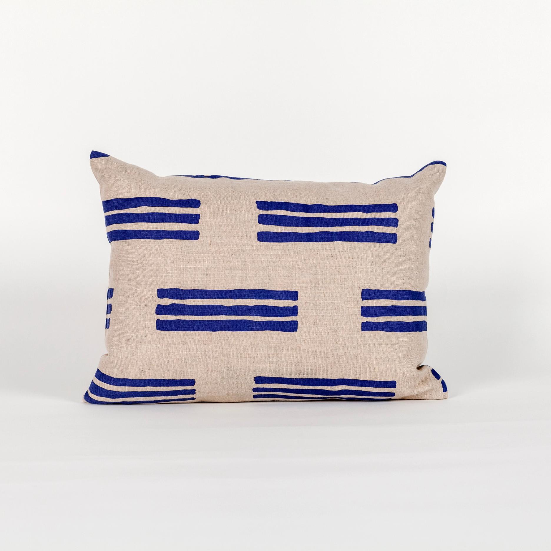 A wide rectangular pillow made of light brown fabric with a minimal pattern of blue horizontal stripes in groups of 3