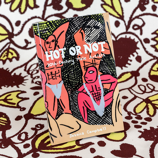 A photograph of a book standing upright against fabric yardage consisting of brown and yellow floral motifs. The book is titled "Hot or Not: 20th-Century Male Artists" by the artist and author Jessica Campbell. The cover features a cartoon version of Pablo Picasso's Cubist painting, "Les Demoiselles d’Avignon," but with chiseled male figures wearing underwear.