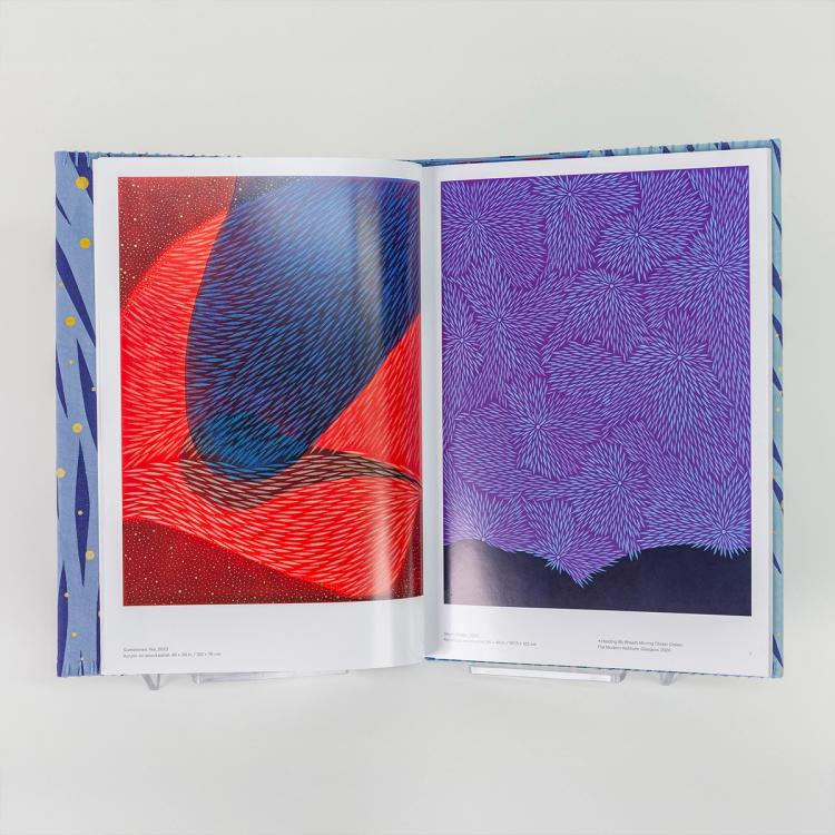 An open hardback book displaying two abstract paintings—on the left, a red and black composition with fine diagonal strokes of blue; on the right, a purple field filled with radiating clusters of fine blue lines.