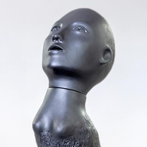 A detail of a small sculpture of a creature composed of a human head looking upwards with a bird's body.
