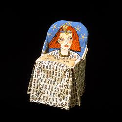 A folding chair covered by the seat cover sits against a black background. The seat cover is printed with a stylized illustration of Rita Hayworth dressed in Egyptian clothing and accessories, against a blue background with abstract yellow stars.