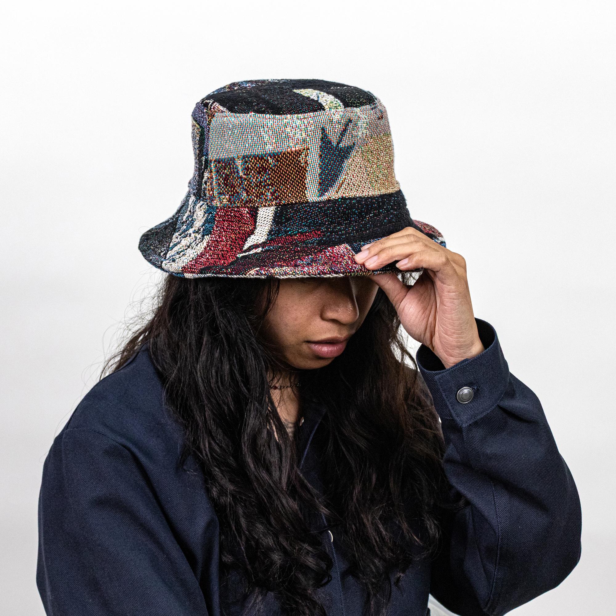 A model wearing a jacquard-woven bucket hat depicting textures, colors, and symbols of computers. This view specifically features a cursor pointing downward on the front of the bucket hat.