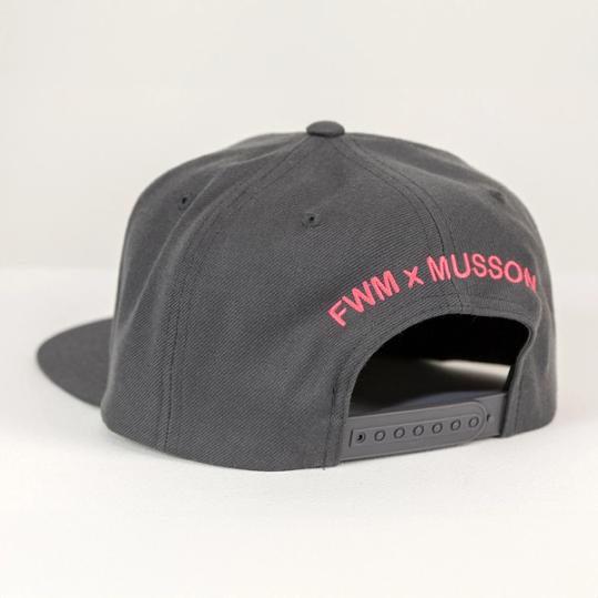 A photograph of the back of a dark grey baseball hat with the words FWM x MUSSON spelled out in red embroidery above a snapback. The cap is at a diagonal facing away from the viewer with the bill just barely visible at the left.