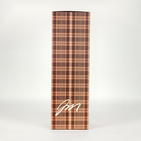 A photo of a tall brown plaid box with the artist Jayson Musson's signature on its lower register.
