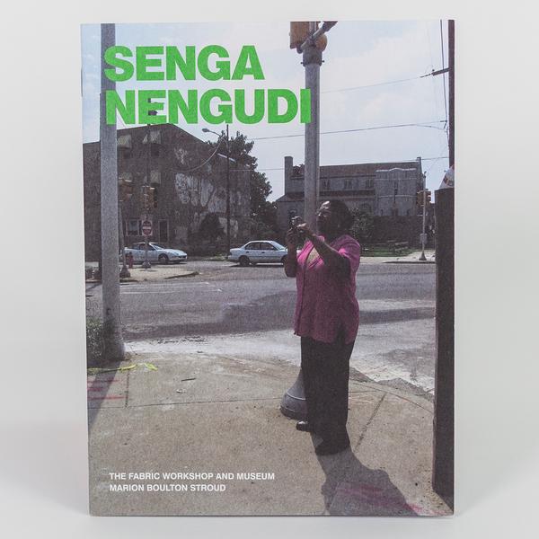 A photo of a book cover featuring a person standing on a street corner taking a photo. In green is the name of the artist and book title, "Senga Nengudi"