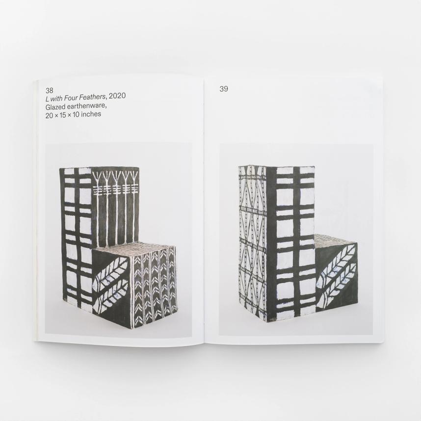 An image of a book spread featuring two photos of black and white painted "L" shaped pedestals with different geometric patterns on each side. There is one image on each page. There is a credit line on the left page and reads: "L with Four Feathers, 2020 Glazed earthenware, 20 x 15 x 10 inches."